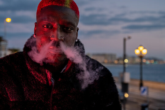 Black man smoking cigarette on waterfront at sunset