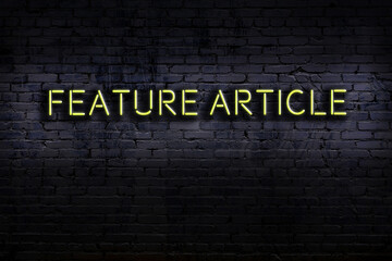 Night view of neon sign on brick wall with inscription feature article