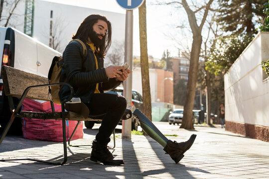 Guy surfing cellphone on street bench