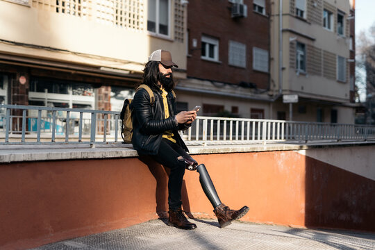Trendy man with artificial limb using phone on street