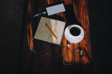 Black smartphone with light screen, paper notebook, pen, headphone and cup of coffee lies on a...