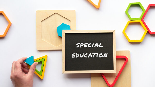 Text Special Education on white blackboard. Nested wood triangles and hexagons in rainbow colors. Turquoise triangle in human hand. Flat lay on white.
