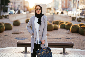 Stylish woman in hijab standing with bag and smartphone