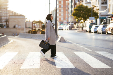 Stylish woman with bag walking on pedestrian crossing