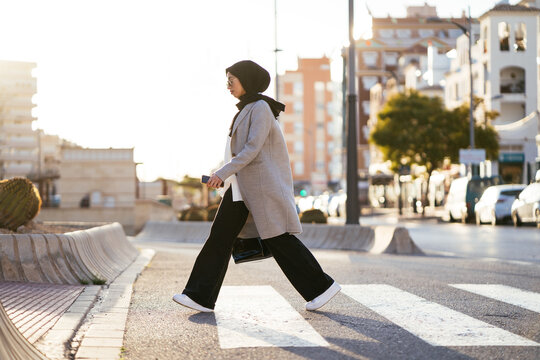Stylish woman in headscarf crossing road on crosswalk