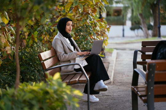 Thoughtful Muslim woman working on laptop in park