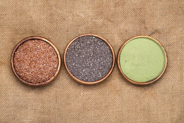 flax seeds, super green powder and chia seeds in wooden bowls on burlap.