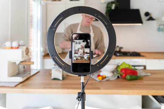 Senior man cooking while filming with phone at home