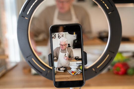 Senior man cooking while filming with phone at home