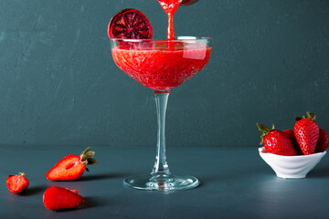 Anonymous hand is pouring strawberry cocktail or juice from mug or shaker. Includes copy space.