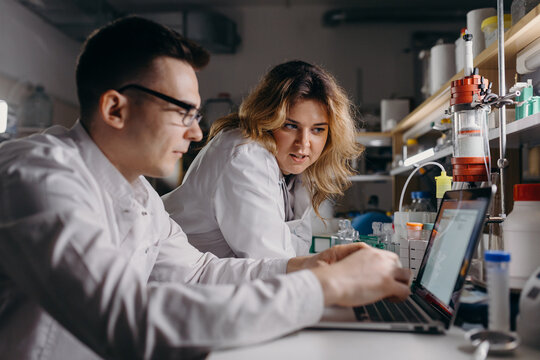 Researcher typing on laptop near colleague in lab