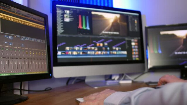 A man working as an editor in a media studio editing video and audio on multiple screens