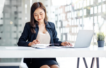 Charming Asian businesswoman sitting in the office with a digital laptop computer. Excited Asian...