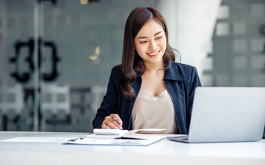 Charming Asian businesswoman sitting in the office with a digital laptop computer. Excited Asian...