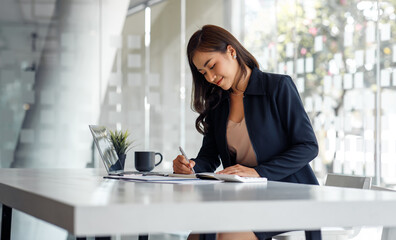 Charming Asian businesswoman sitting in the office with a digital laptop computer. Excited Asian businesswoman raising hands to congratulate while working in a modern office,