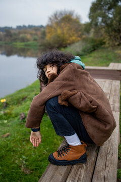 Teenager squatting on a border by the river
