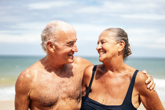 Portrait Of A Smiling Elderly Couple On The Beach Looking At Each Other