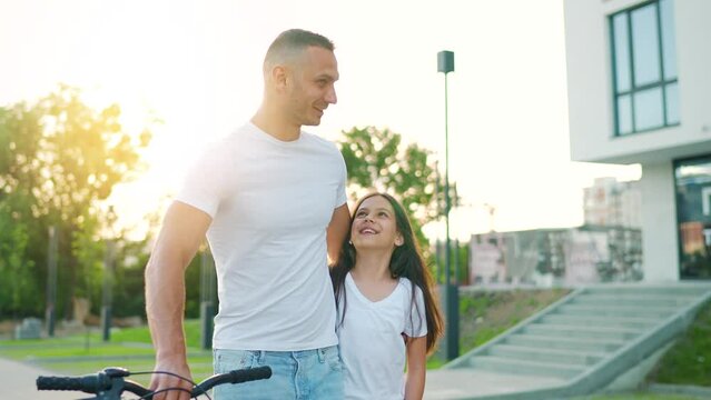 Dad and daughter walk around their area at sunset. Child holds father's hand. Slow motion