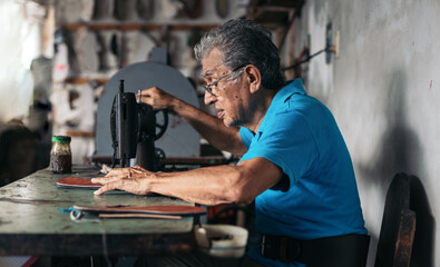 Older shoemaker sewing a sole