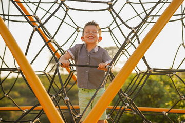 Niño feliz contento jugando en el parque disfrutando escalando subiendo en los juegos infantiles...