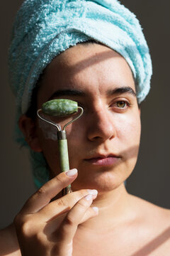 Portrait of cute naked woman using jade roller on face