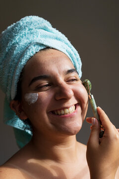 Portrait of cute naked woman using jade roller on face