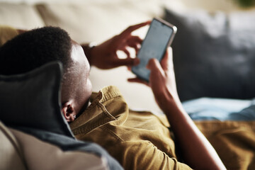 Let me engage in some chats here. Cropped shot of an unrecognizable man using a smartphone while relaxing on his couch at home.