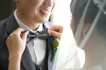 the bride helps put the bow tie on the groom