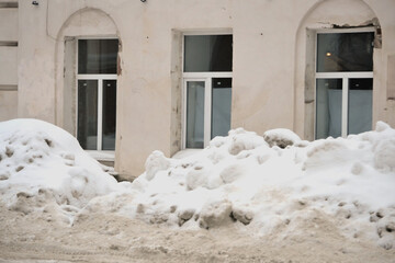 Gloomy winter cityscape. Snowdrifts on the edge of the street near the stone wall of the old...
