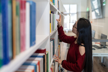 Female college student in library. Concentrated young woman picking books for preparing for exam,...