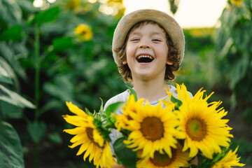 Happy little boy walking in field of sunflowers. Child playing with big flower and having fun. Kid...