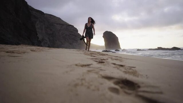 Slow motion of young woman freelance creative photographer walking barefoot on sandy tropical beach with scenic ocean seascape