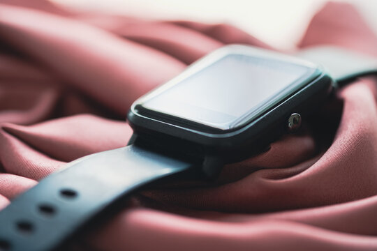 A Black Smart Watch Rests On A Pink Cloth.