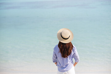Rear view image of a woman with hat walking on the white beach and blue sea