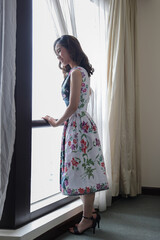 Beautiful young woman wearing modern cheongsam inspired dress standing posing next to window light