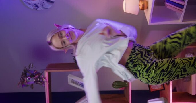 Vertical video of woman recording dance video in living room. Young female student or teenager dancing at home for musical clip. Blogger making music content for channel, wearing elf ears.