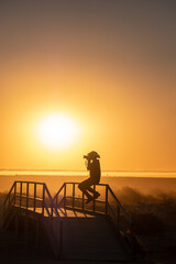 Fototapeta premium silhouette of a person on a bridge taking photo with sunset background.