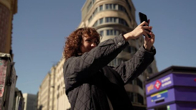 Curly Caucasian Woman Taking Selfie With Smartphone In City Center