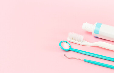 dental instruments, toothbrush and paste on pink background