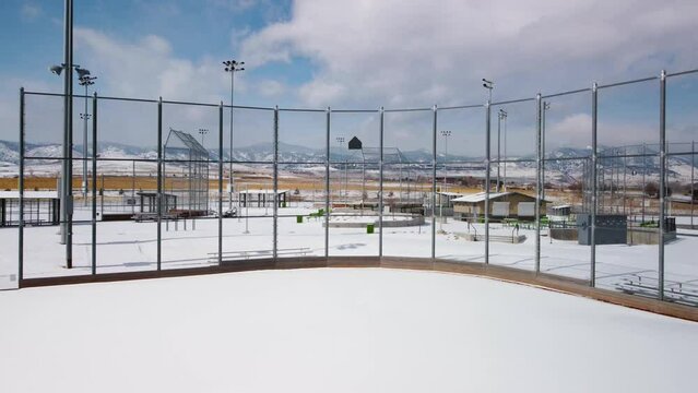 Reveal of baseball and softball field during the winter with fresh snow in front of the Colorado Rocky Mountains, aerial