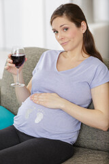 Obraz na płótnie Canvas smiling pregnant woman drink glass of wine at home