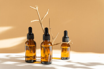 Mock-up of three amber glass bottles with dropper lid on beige background with floral shadow....
