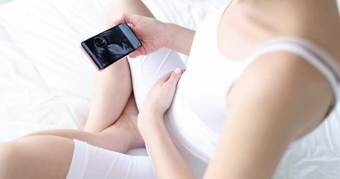 Pregnant woman looks into smartphone at ultrasound of child