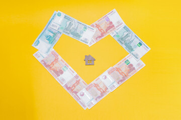 Ivanovo, Russia - 03.03.2022:a miniature of a wooden house lies in the middle of Russian banknotes in the shape of a heart: real estate services for the purchase of real estate and own housing, exchan