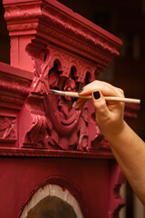 Hand painting wooden cupboard with dazzling handmade carved ornaments in red color with paint brush...
