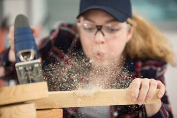 female carpenter blows off wood dust