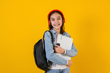 portrait of young hispanic child teen girl student with headphones listening music on a yellow...