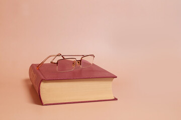 Reading glasses lie on a thick book, colored background. Side view