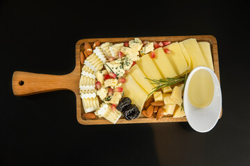 Various types of cheese served on a wooden board with dry plum and almonds