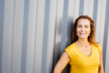 elder woman leaning against gray metal wall with copy space